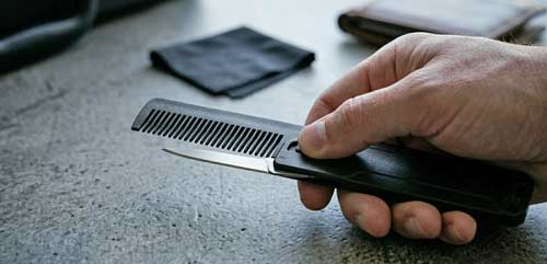 A black polymer pocket comb being held as a small blade is partially extended from the side of the handle