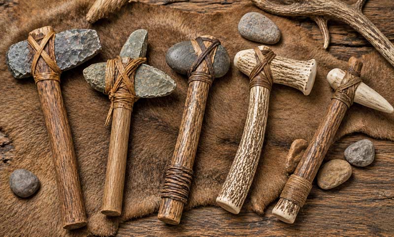 Early stone, bone, and antler tomahawks displayed on an animal hide.