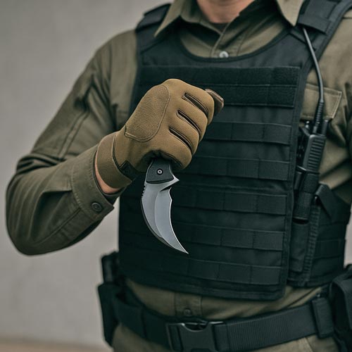 Person in tactical gear holding a karambit knife.