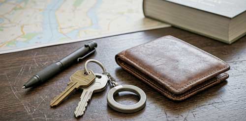 Tactical pen and keychain defense tool on a wooden table next to a wallet and keys.