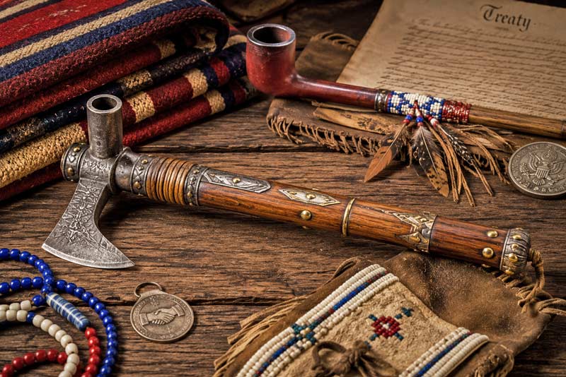 Decorative pipe tomahawk displayed with ceremonial items and a historical treaty document.