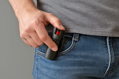 Pepper spray clipped to a jeans pocket with a hand gripping it.