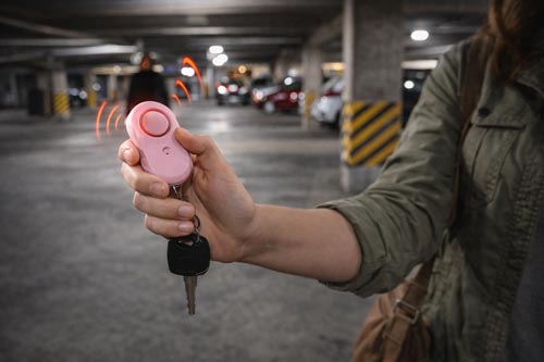 Woman holding a personal safety alarm in a dimly lit hotel hallway.