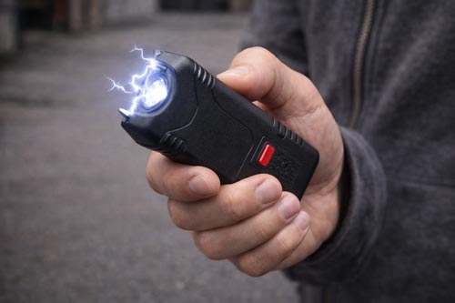 Hand holding a compact stun gun with visible electric arc