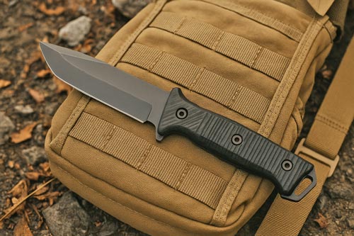 tactical fixed blade knife resting on a tan tactical backpack outdoors